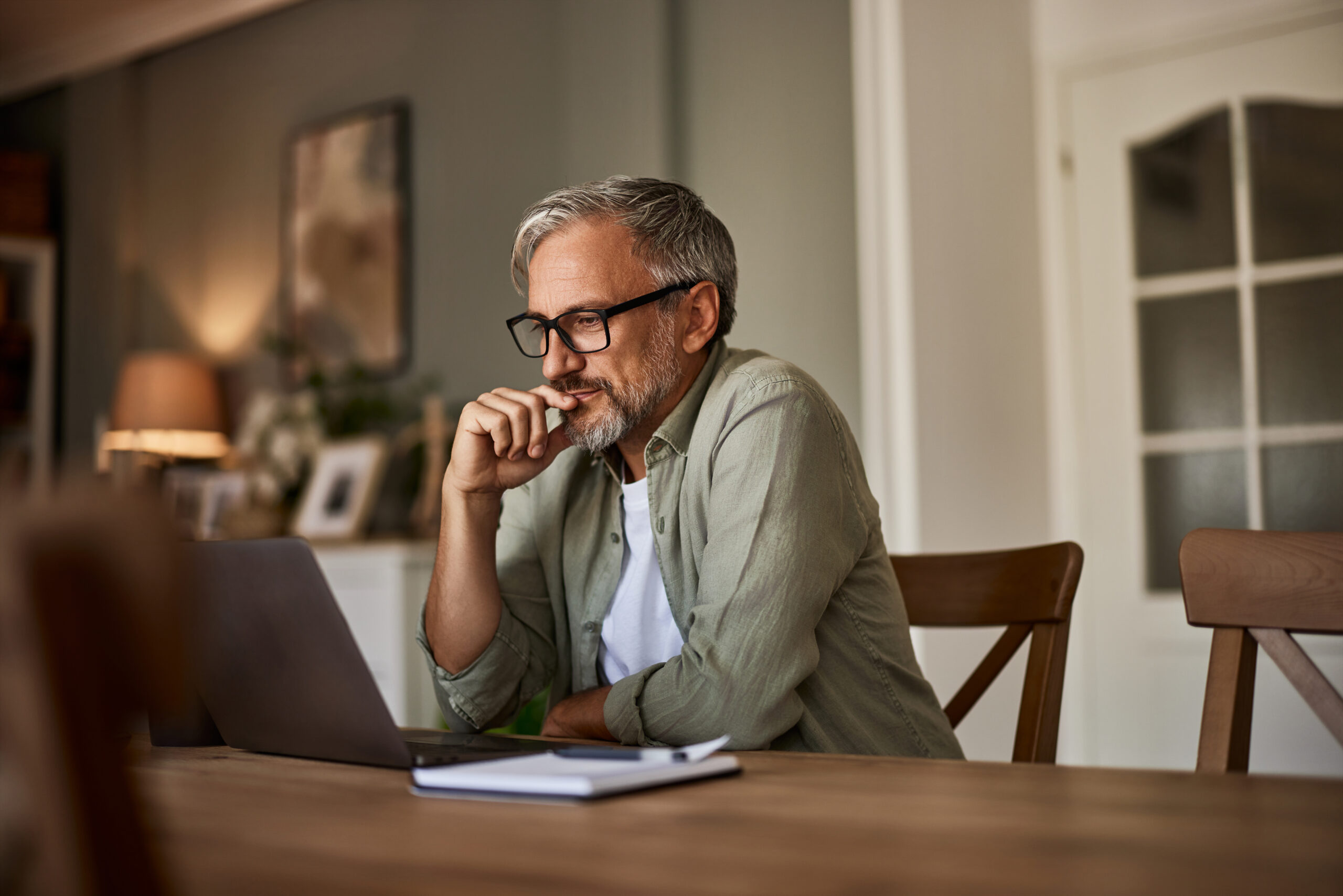 a confident senior male freelancer reading an online document on a laptop.